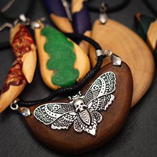 A scattered collection of metal charms, including a skull, a raven, and an ampersand, resting on a scorched and gnarled wood surface.
